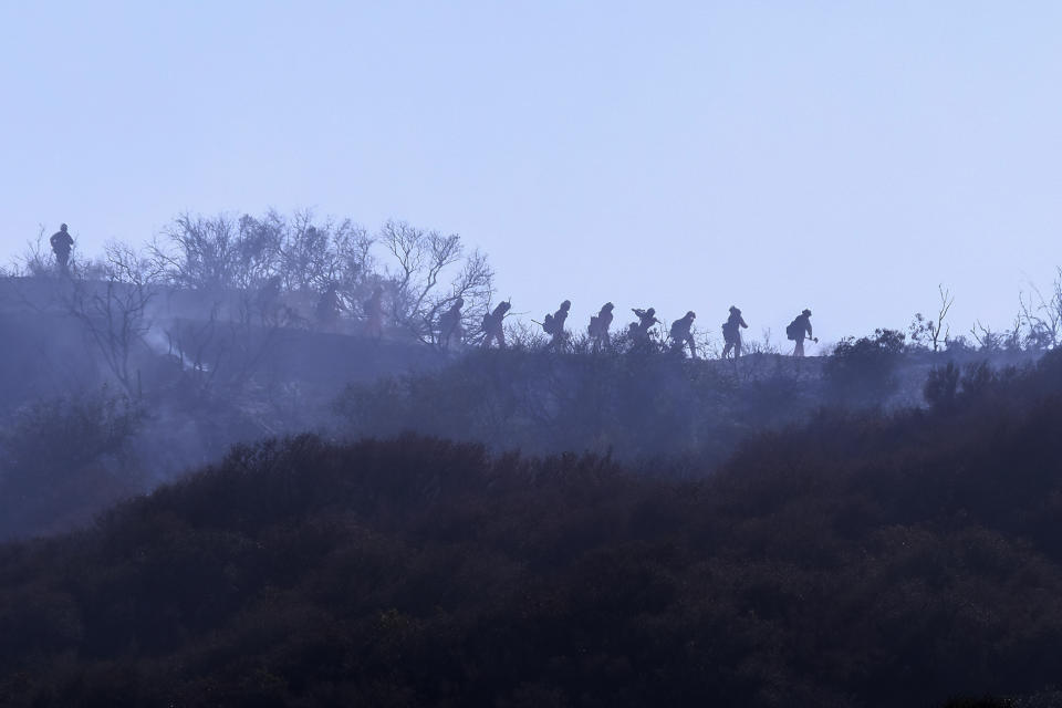 A hotshot hand crew walks in line during a wildfire in Topanga, west of Los Angeles, Monday, July 19, 2021. A brush fire scorched about 15 acres in Topanga today, initially threatening some structures before fire crews got the upper hand on the blaze, but one firefighter suffered an unspecified minor injury. (AP Photo/Ringo H.W. Chiu)