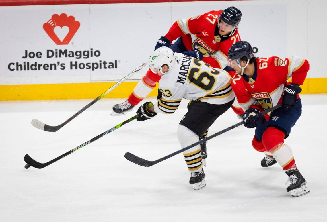 Florida Panthers center Eetu Luostarinen (27) and defenseman Brandon Montour (62) try to get the puck from Boston Bruins left wing Brad Marchand (63) during the third period of a game on Tuesday, March 26, 2024, at Amerant Bank Arena in Sunrise, Fla.