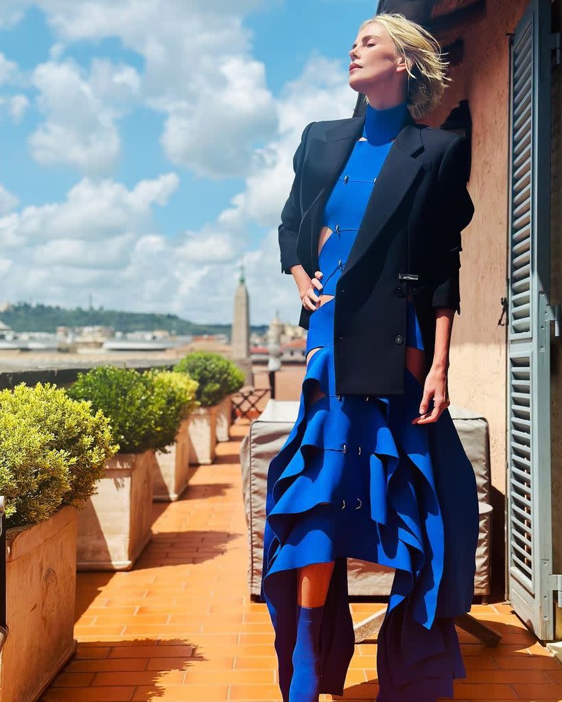 Charlize posing in her blue dress with a black blazer behind her is a vista of Rome