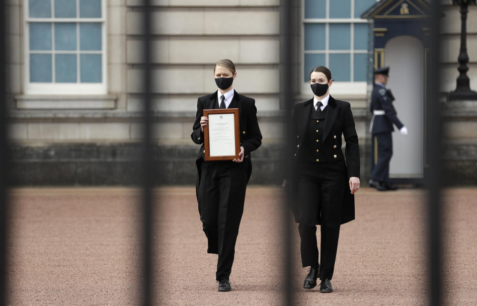 A member of staff carries an announcement, regarding the death of Britain's Prince Philip, to be displayed on the fence of Buckingham Palace in London, Friday, April 9, 2021. Buckingham Palace officials say Prince Philip, the husband of Queen Elizabeth II, has died. He was 99. Philip spent a month in hospital earlier this year before being released on March 16 to return to Windsor Castle. (AP Photo/Matt Dunham)