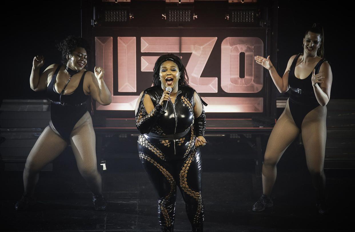 Lizzo performing at the Palace Theatre, St. Paul, in the center a dancer on both sides, all wearing black costumes, surrounded by shadowing and lights