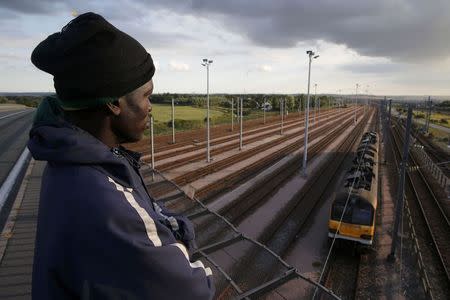 A migrant from Rwanda, who gave his name as Alex, aged 35 and is the father of two children, stands on an overpass as he watches a train pass on tracks below in Calais, France, July 30, 2015. REUTERS/Pascal Rossignol