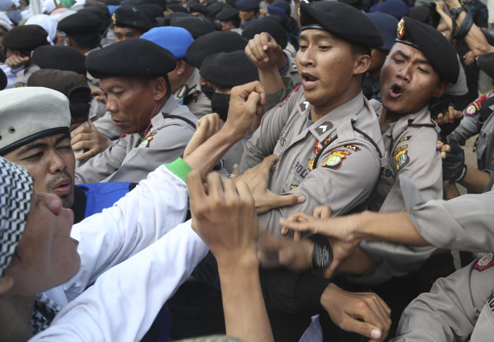 FILE - In this Nov. 22, 2013, file photo, Indonesian police officers block members of the militant Islamic Defenders Front (FPI) during a demonstration outside Australian Embassy in Jakarta. The Islamic Defenders Front, better known for vigilante actions against gays, Christmas decorations and prostitution, has over the past decade and a half repurposed its militia into a force that's as adept at searching for victims buried under earthquake rubble and distributing aid as it is at inspiring fear. (AP Photo/Tatan Syuflana, File)