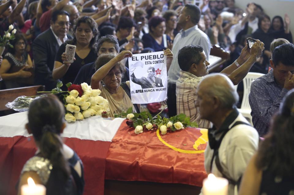 A woman holds up an image of Peru's late President Alan Garcia next to his coffin on the second day of his wake at his party's headquarters in Lima, Peru, Thursday, April 18, 2019. Garcia shot himself in the head and died Wednesday as officers waited to arrest him in a massive graft probe that has put the country's most prominent politicians behind bars and provoked a reckoning over corruption. (AP Photo/Martin Mejia)