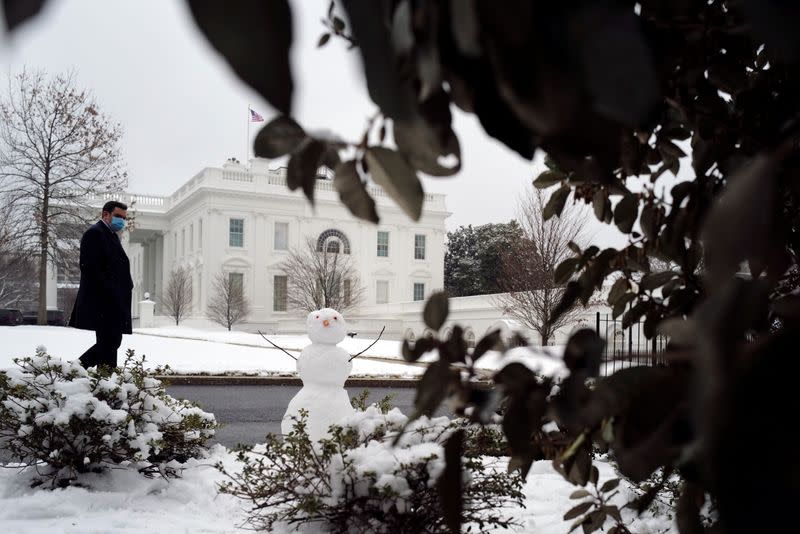 A man walks past a snowman near the White House in Washington