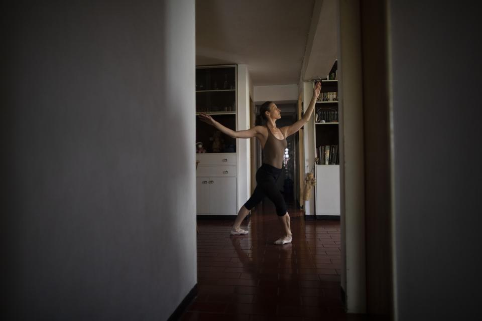 Carolina Wolf, who dances with Venezuela's national ballet, trains in her living room, during a lockdown to curb the spread of COVID-19 in Caracas, Venezuela, Tuesday, Aug. 11, 2020. The 42-year-old ballerina said her living room is four times smaller than the studio where she practiced daily at the famed Teresa Carreño Theater, and she doesn't dare do jumps in fear of injuring herself on the hard floor. (AP Photo/Ariana Cubillos)