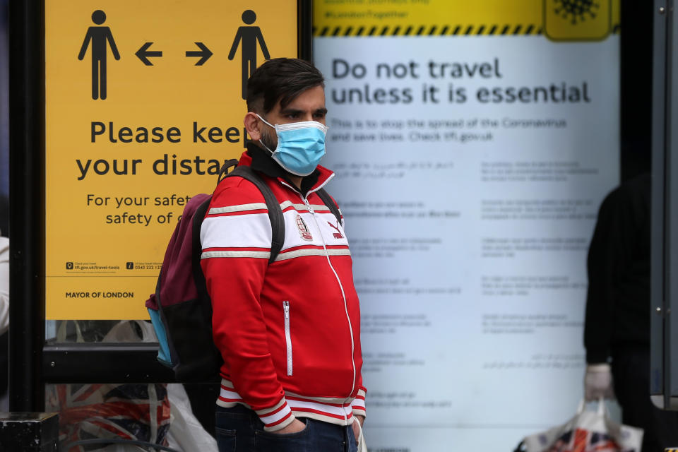 A man wearing a protective face mask waits at a bus stop surrounded by information on social distancing in Camden in central London on May 11, 2020, as life in Britain continues during the nationwide lockdown due to the novel coronavirus pandemic. - British Prime Minister Boris Johnson on May 10 announced a phased plan to ease a nationwide coronavirus lockdown, with schools and shops to begin opening from June 1 -- as long as infection rates stay low. Starting this week, he said the government would be "actively encouraging" people to return to work where they could not do so from home, for example in manufacturing or construction. (Photo by ISABEL INFANTES / AFP) (Photo by ISABEL INFANTES/AFP via Getty Images)