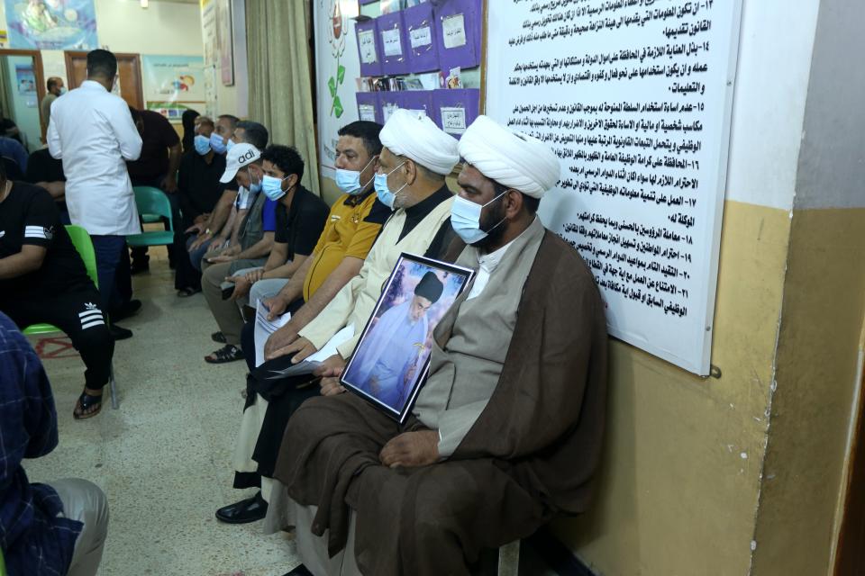 A follower of populist Shiite cleric Muqtada al-Sadr holds a picture of him while waiting with others to receive a dose of the Chinese Sinopharm coronavirus vaccine at a clinic in Sadr City, Baghdad, Iraq, Wednesday, May 4, 2021. Iraq’s vaccine rollout had been faltering for weeks. Apathy, fear and rumors kept many from getting vaccinated despite a serious surge in coronavirus infections and calls by the government for people to register for shots. It took al-Sadr’s public endorsement of vaccinations — and images of him getting the shot — to turn things around. (AP Photo/Hadi Mizban)