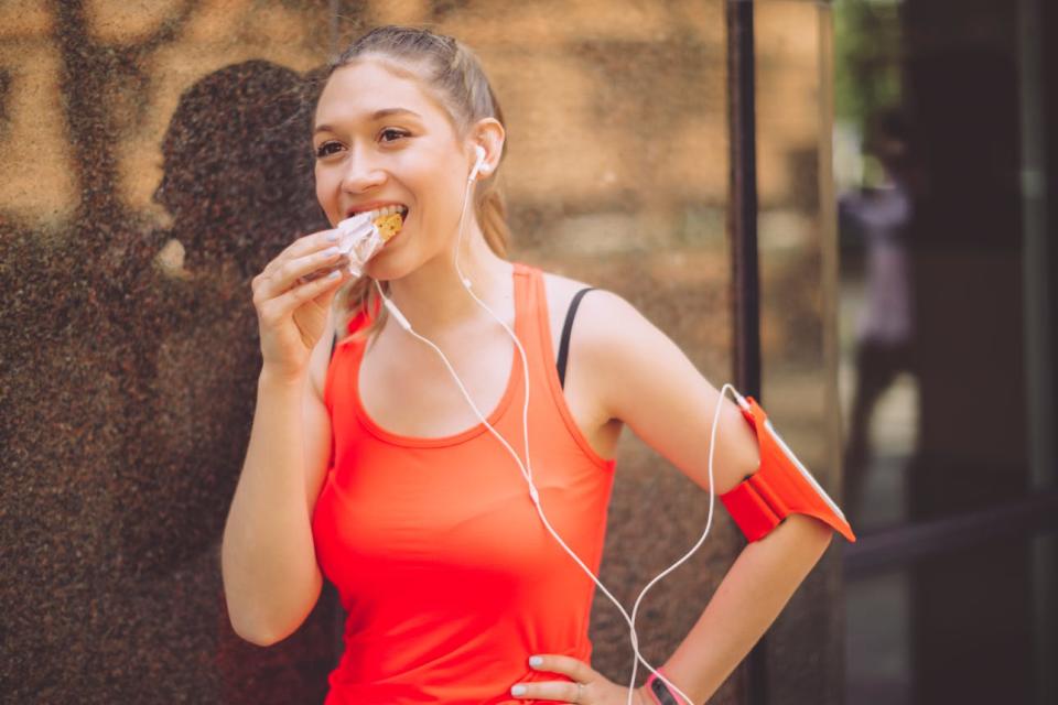 A woman takes a break from exercising to eat a granola bar