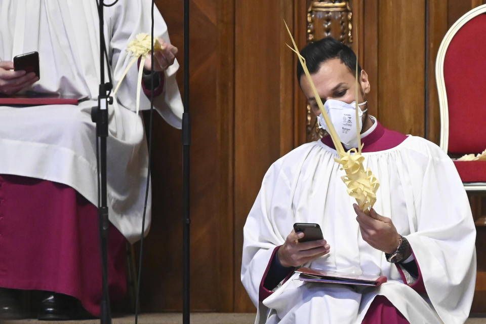 A prelate wearing a face mask holds a smartphone and a palm branch prior to the Pope's Palm Sunday Mass behind closed doors in St. Peter's Basilica, at the Vatican, Sunday, April 5, 2020, during the lockdown aimed at curbing the spread of the COVID-19 infection, caused by the novel coronavirus. (AP Photo/pool/Alberto Pizzoli)