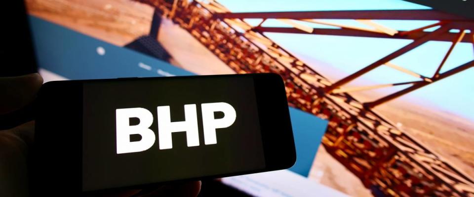 Person holding smartphone with logo of mining, metals and petroleum company BHP Group on screen in front of website.