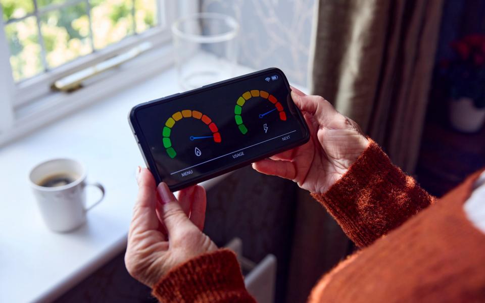 Senior Woman With Smart Meter Trying To Keep Warm By Radiator