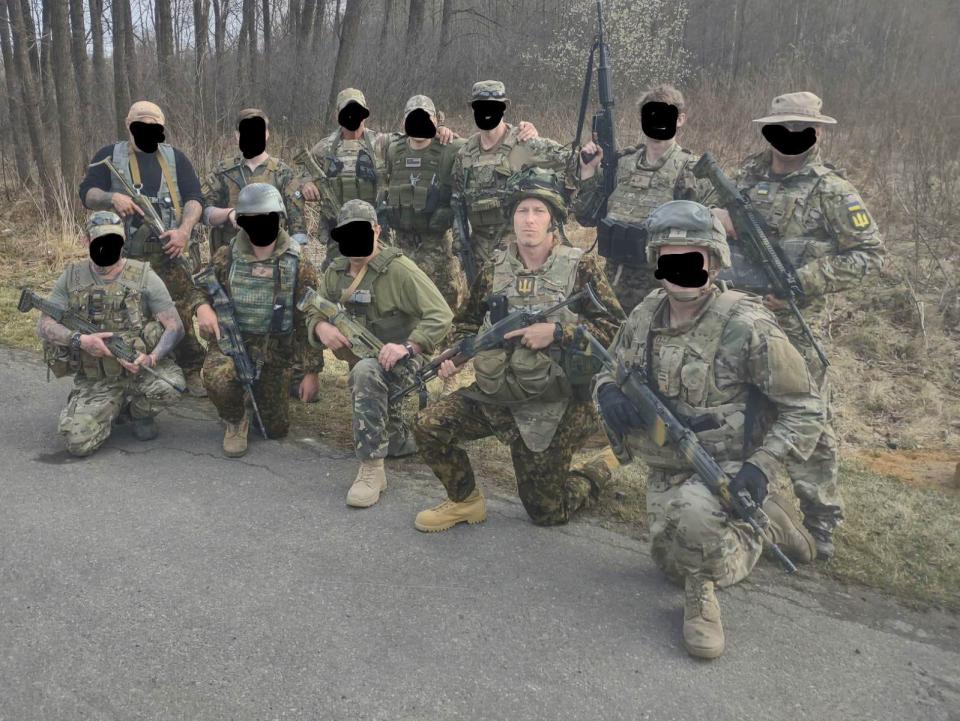 Tristan Nettles, wearing gear with Ukraine's national symbol on his chest, kneels with other volunteers (faces obscured) during training to fight against Russia's invasion of Ukraine.