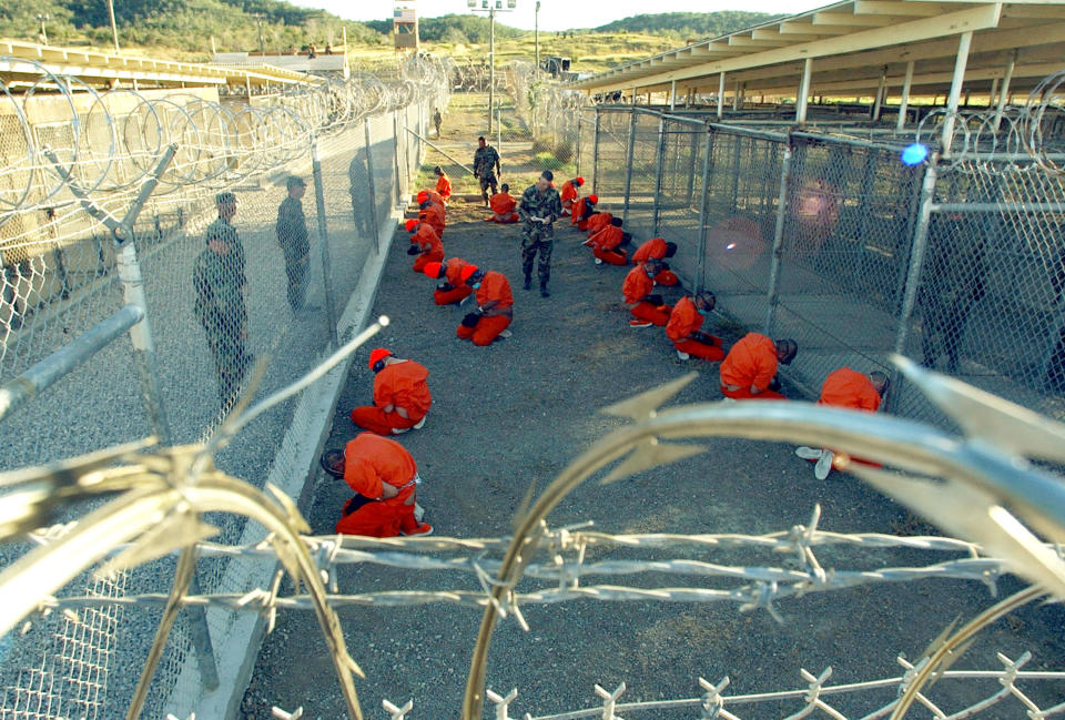 U.S. Military Police guard Taliban and al Qaeda detainees in orange jumpsuits January 11, 2002 in a holding area at Camp X-Ray at Naval Base Guantanamo Bay, Cuba during in-processing to the temporary detention facility. The detainees will be given a basic physical exam by a doctor, to include a chest x-ray and blood samples drawn to assess their health, the military said. The U.S. Department of Defense released the photo January 18, 2002. (Photo by Petty Officer 1st class Shane T. McCoy/U.S. Navy/Getty Images)