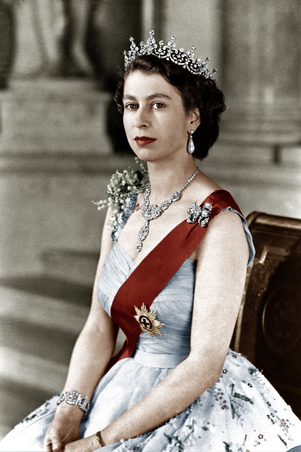 <p>In a sleeveless and embellished blue dress, diamond earrings, necklace, and a bracelet–topped off with a sparkly diamond tiara. </p>