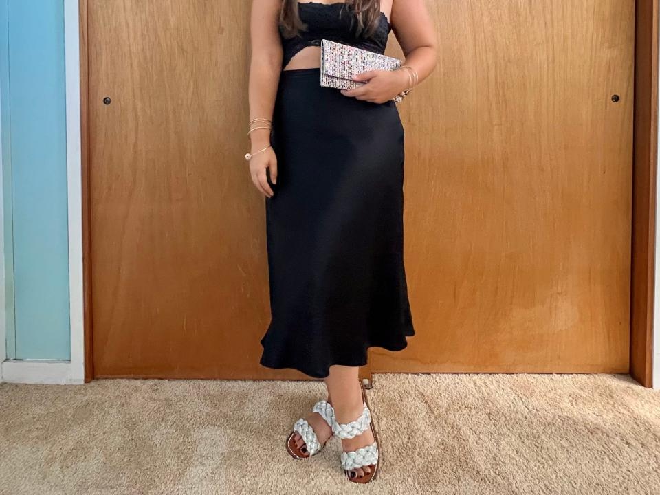 Author posing in black two-piece dress, black wide-brimmed hat, white clutch, and white sandals.