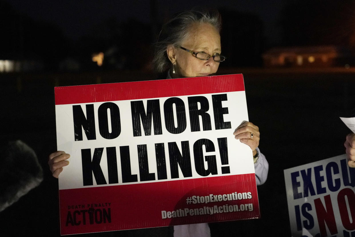 Sally Fran Ross, a retired United Methodist minister, left, holds a protest sign at the small prayer vigil at the Mississippi State Penitentiary in Parchman, Miss., prior to the scheduled execution of David Neal Cox, 50, Wednesday, Nov. 17, 2021. Cox, who killed his estranged wife and terrorized their family in 2010, was scheduled to receive a lethal injection Wednesday evening at the penitentiary. (AP Photo/Rogelio V. Solis)