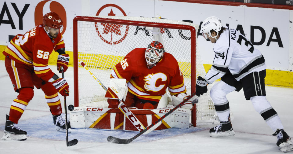 Los Angeles Kings forward Arthur Kaliyev, right, tries to get to the puck as Calgary Flames goalie Jacob Markstrom, center, blocks the net and defenseman MacKenzie Weegar tries to clear the puck during the third period of an NHL hockey game Tuesday, March 28, 2023, in Calgary, Alberta. (Jeff McIntosh/The Canadian Press via AP)