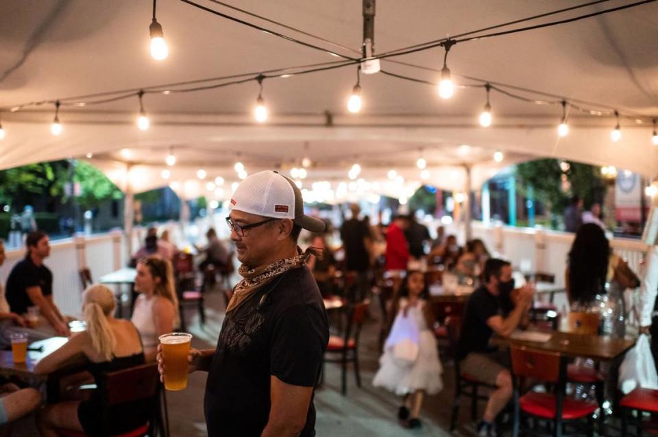 Ron Pili, a resident of the neighborhood, drinks with friends in July 2020 under a tent on the 1400 block of R Street in Sacramento, which was closed to vehicles to give restaurants and bars room to seat outdoors for pandemic social distancing.