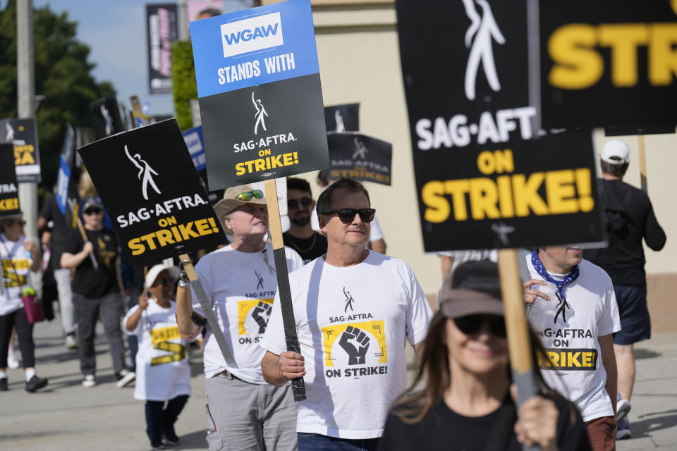 WGA and SAG-AFTRA member Michael Hitchcock, center, carries a sign on the picket line outside Paramount Pictures studio on Wednesday, Sept. 27, 2023, in Los Angeles. Hollywood's writers strike was declared over Tuesday night when board members from their union approved a contract agreement with studios, bringing the industry at least partly back from a historic halt in production. The actors strike continues in their bid to get better pay and working conditions. (AP Photo/Chris Pizzello)