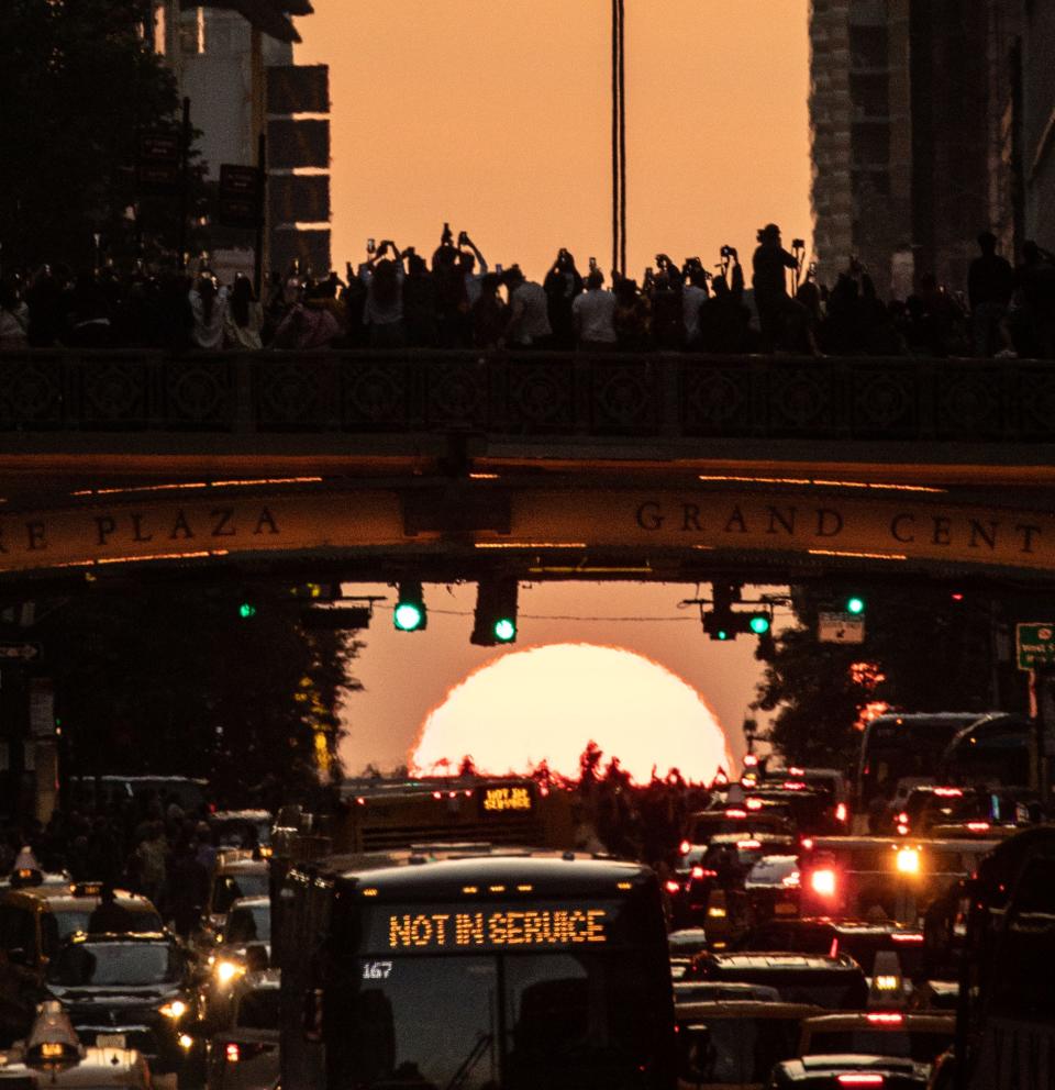 People stand on an overpass over 42nd St. in Manhattan May 30, 2023 as they watch and photograph the setting sun during the second consecutive night of Manhattanhenge. Manhattanhenge is an event during which the setting sun is aligned with the east-west streets of the street grid of Manhattan. The phenomenon occurs over two days, twice each year. There was partial Manhattanhenge Monday night. The second Manhattanhenge of 2023 will occur on July 12 and 13. Smoke from Canadian wildfires is responsible for the orange haze.