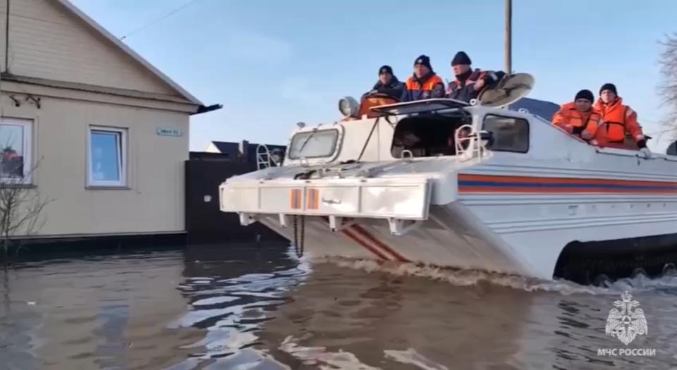 In this grab taken from a video released by the Russian Emergency Ministry Press Service on Saturday, April 6, 2024, emergency workers aboard an amphibious vehicle look to evacuate local residents after a part of a dam burst causing flooding, in Orsk, Russia. (Russian Emergency Ministry Press Service via AP)