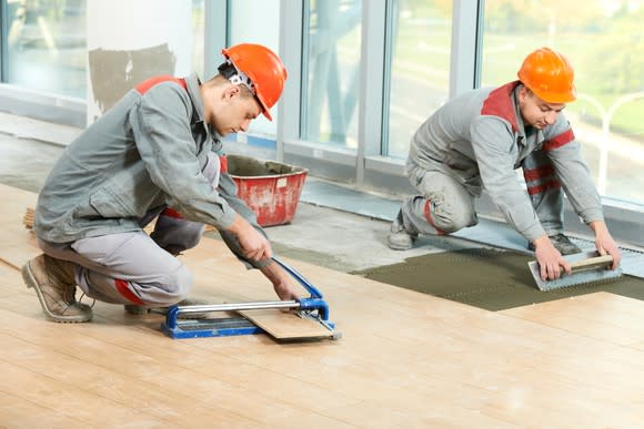 Two construction workers laying flooring.