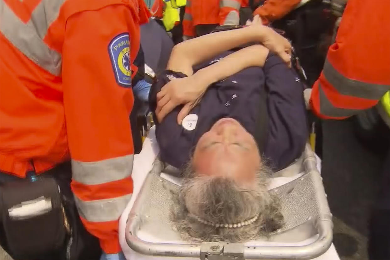 In this image taken from a video footage run by TVB, a woman is taken away on a stretcher in the aftermath of an accident where four passenger buses and a truck collided near a Hong Kong road tunnel on Friday, March 24, 2023. Dozens were injured, including children. Most of the injuries were minor. (TVB via AP)