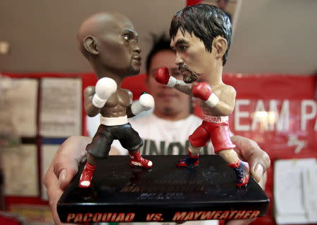 A store employee holds up a stand with miniature figurines of boxers Manny Pacquiao (R) of the Philippines and Floyd Mayweather Jr. of the U.S., at a mall in Manila April 23, 2015. Pacquiao is scheduled to fight Mayweather on May 2, 2015 in Las Vegas, Nevada. REUTERS/Romeo Ranoco