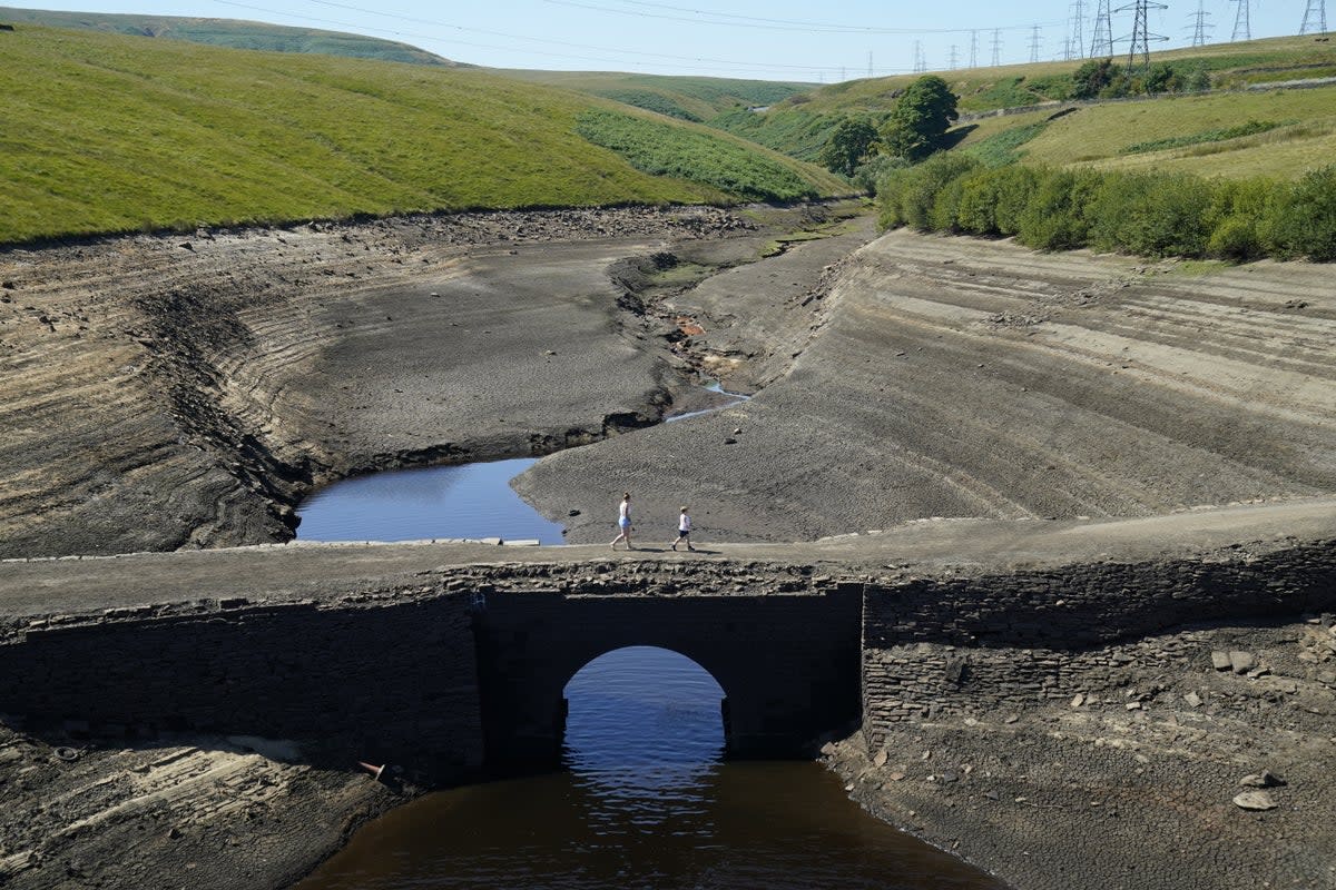 People walk across the dry cracked earth at Baitings Reservoir in Ripponden, West Yorkshire, where water levels are significantly low (Danny Lawson/PA) (PA Wire)