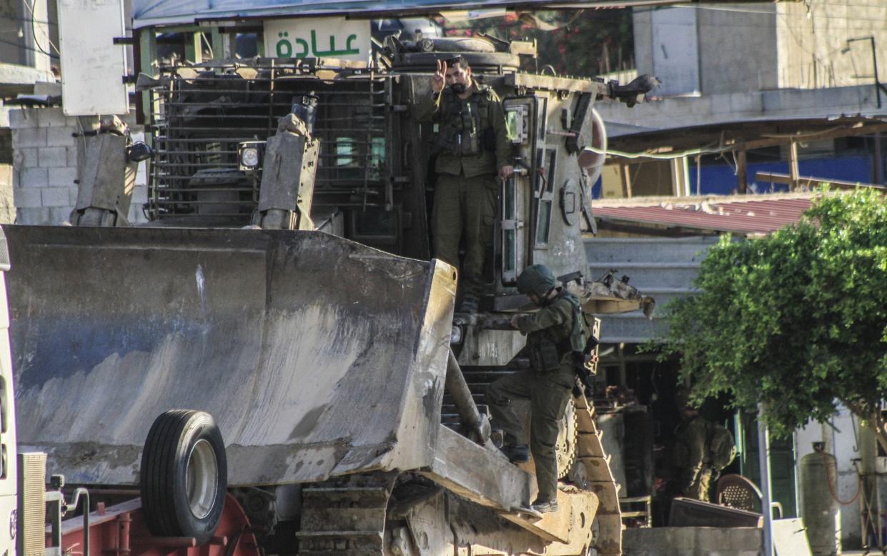 Israeli soldiers climb onto an armored military bulldozer near the Al-Far'a refugee camp