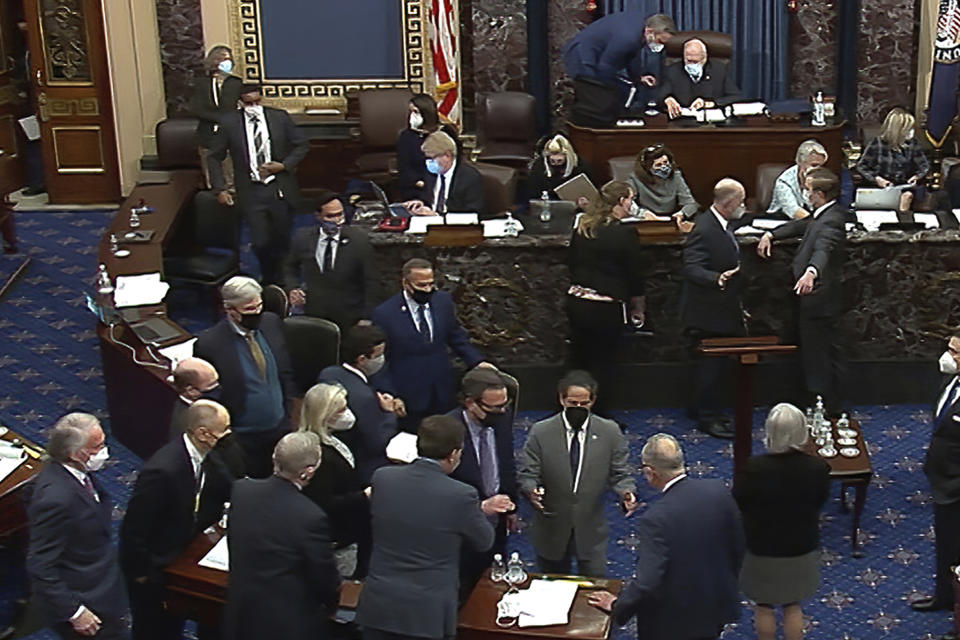 In this Feb. 10, 2021, image from video, Senate parliamentarian Elizabeth MacDonough, seated in the back second row third from right, talks as senators gather in the foreground around Senate Majority Leader Chuck Schumer of N.Y., and House impeachment manager Rep. Jamie Raskin, D-Md., bottom left, during the second impeachment trial of former President Donald Trump in the Senate at the U.S. Capitol in Washington. MacDonough has guided the Senate through two impeachment trials, vexed Democrats and Republicans alike with parliamentary opinions and helped rescue Electoral College certificates from a pro-Trump mob ransacking the Capitol.(Senate Television via AP)