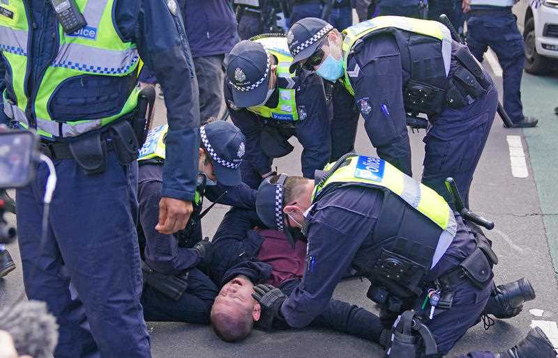 Police officers detain a man as protesters gather outside Parliament House in Melbourne.