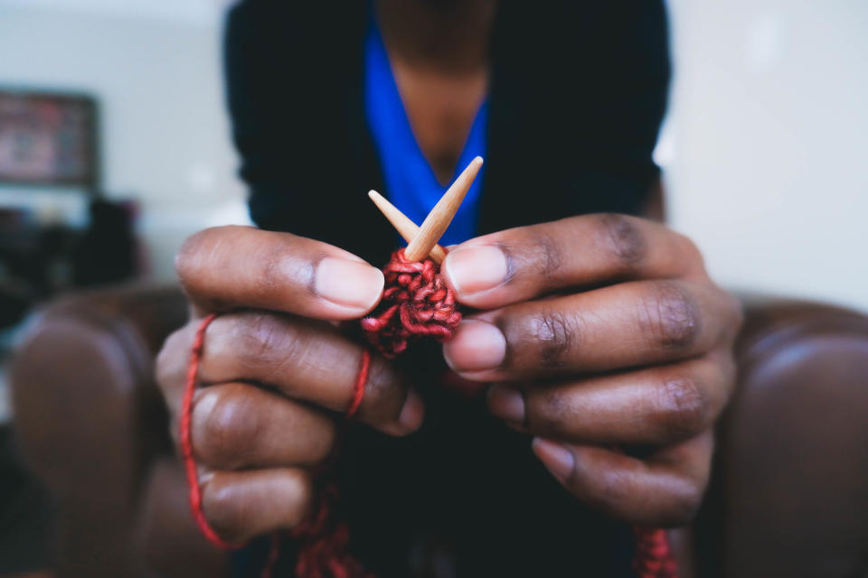 A close-up shot of hands holding knitting needles with red yarn