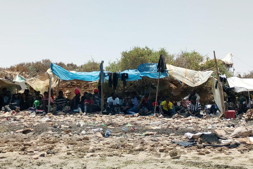 In this photo taken by 29-year-old migrant from the Ivory Coast, a group of sub-Saharan Africans is seen stranded on a beach allegedly at the Tunisian-Libyan border on Thursday 6 July 2023. The migrants, including women and small children, told AP by phone they were rounded up by Tunisian authorities since Saturday and progressively dumped on the border where they have been stuck for days. (UGC via AP)