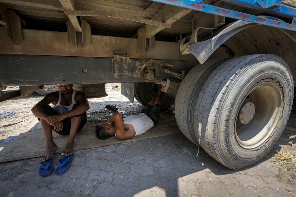 FILE- Workers take refuge from the scorching heat under a parked truck in Guwahati, India, Saturday, May 25, 2024. A monthslong heatwave across swathes of India has killed more than 100 people and led to over 40,000 suspected cases of heat stroke in the last three and a half months, a Health Ministry official said Thursday, June 20. (AP Photo/Anupam Nath, File)