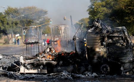 Locals walk past a shell of a burnt out truck used to barricade roads by protesters in Atteridgeville a township located to the west of Pretoria, South Africa June 21, 2016. REUTERS/Siphiwe Sibeko