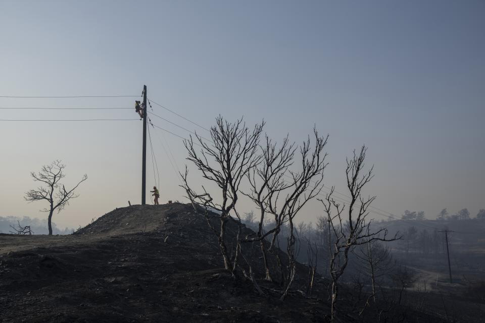 A worker climbing on an electricity pole repairs cables after a wildfire near Gennadi village, on the Aegean Sea island of Rhodes, southeastern Greece, on Wednesday, July 26, 2023. Major fires raging in Greece and other European countries have advanced. The flames have caused additional deaths, destroying homes and threatening nature reserves during a third successive wave of extreme temperatures. (AP Photo/Petros Giannakouris)