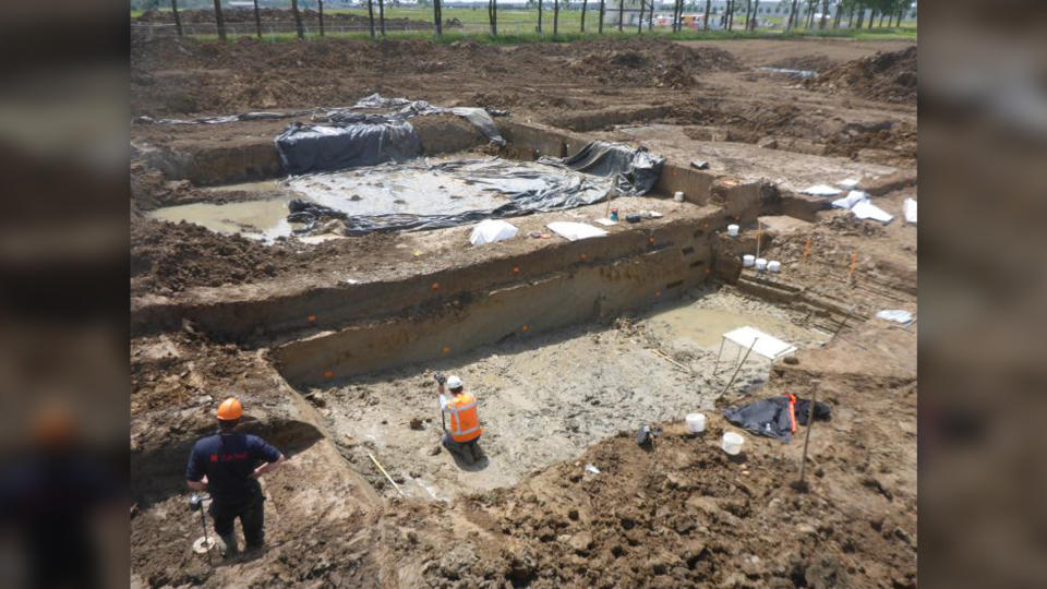 We see two archaeologists excavating a rectangular-cut out in the ground.