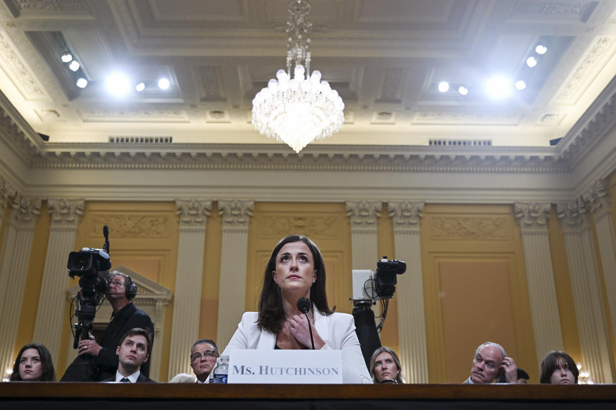 Cassidy Hutchinson, in white, below a chandelier, looks upward.