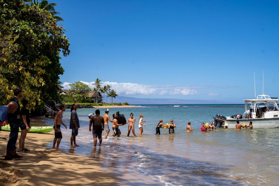 Dozens of local residents of Kahana line up and step into the water to help pass down the supplies to shore in Kahana, Hawaii on August 11, 2023.
