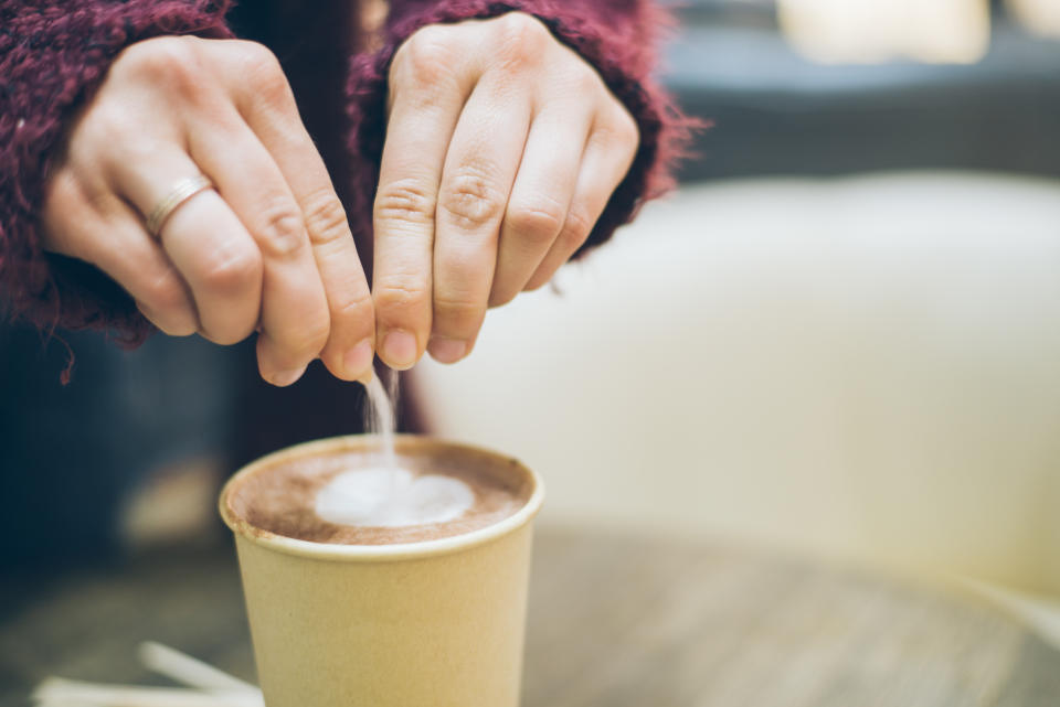 woman hands pouring sugar to the latte cup in cafe