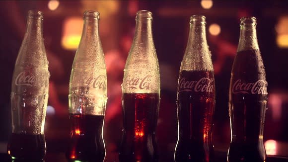 Five Coke bottles with increasing amounts of liquid in them, lined up in a row.