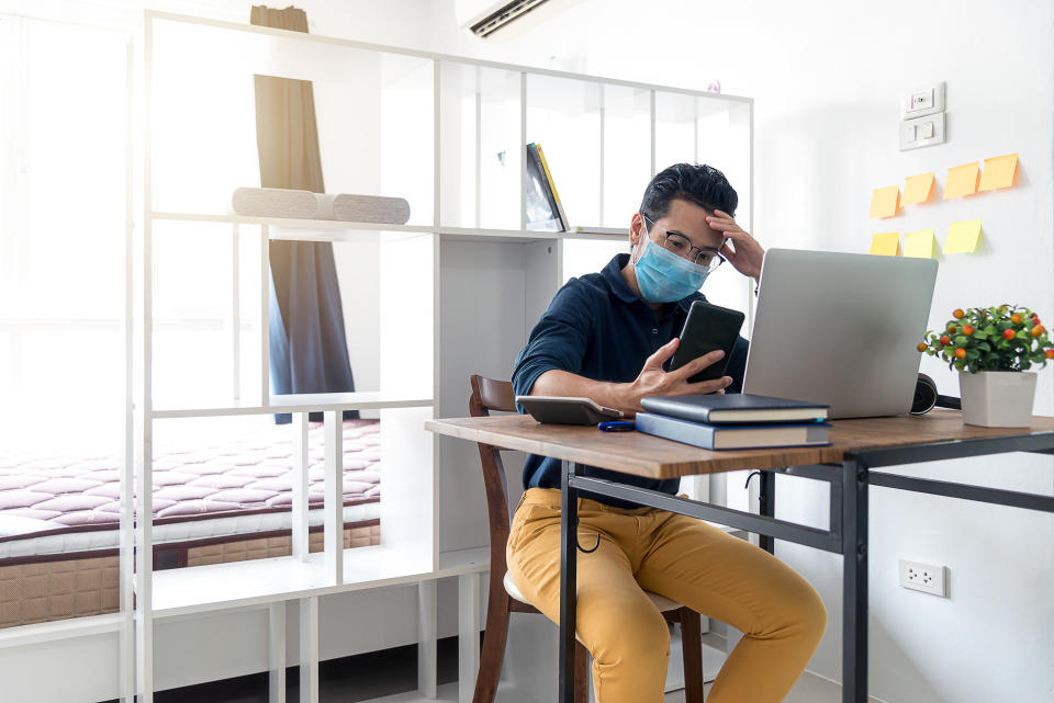 Concentrated Businessman ware mask sitting on working table and looking at Smart phone.  Man working from home during corona virus quarantine.