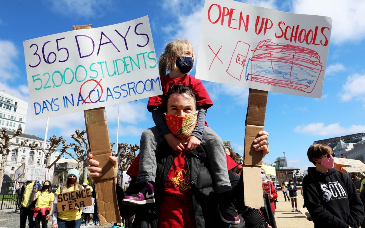 A parent protests with his young daughter on his shoulders and banners in each hand