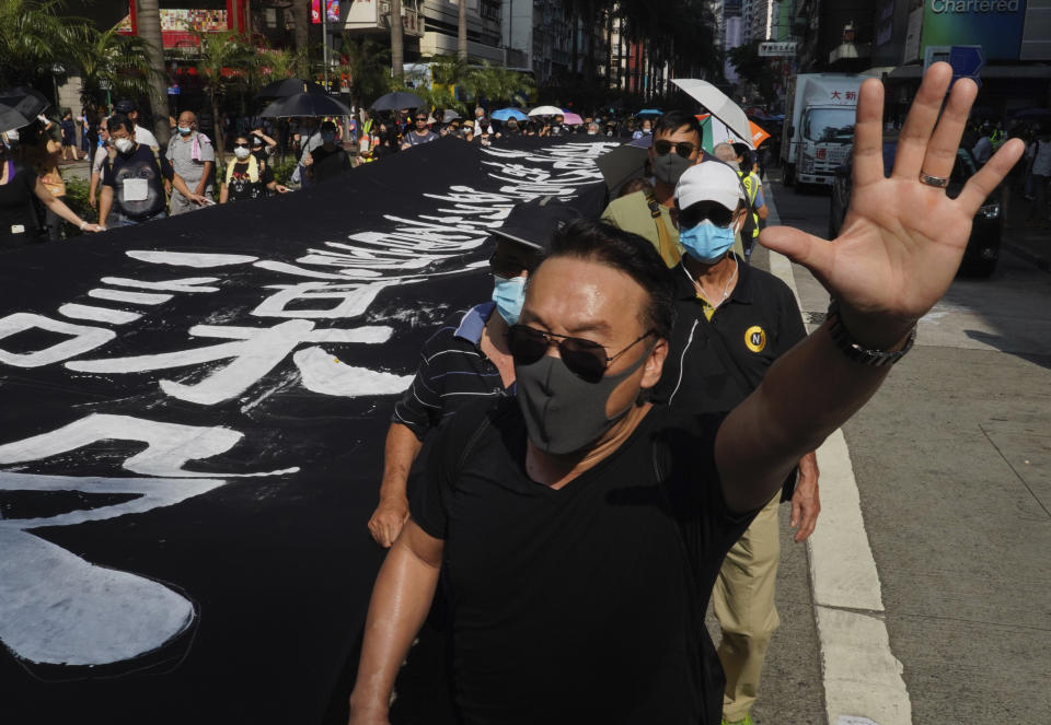 A masked protester holds up his hand to represent the protesters' five demands as he walks next to a banner reading "Hong Kong police deliberately murder" in Hong Kong on Saturday, Oct. 5, 2019. All subway and trains services are closed in Hong Kong after another night of rampaging violence that a new ban on face masks failed to quell. (AP Photo/Vincent Yu)