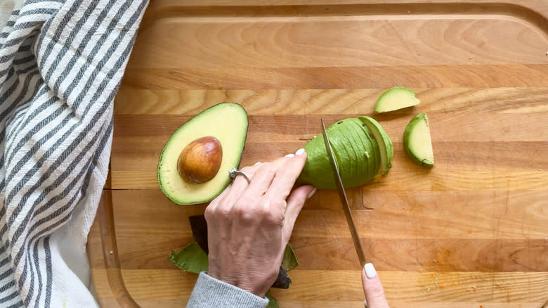 hand slicing avocado on board