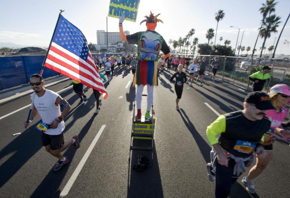 Ed Ettinghausen, from Murrieta, center, sets up about a quarter of a mile from the starting line and jokingly tells the runners that they are almost done, though they have just started their race at the Surf City Marathon/Half Marathon, Sunday, Feb. 2, 2014 in Huntington Beach, Calif. (AP Photo/The Orange County Register, Michael Goulding)