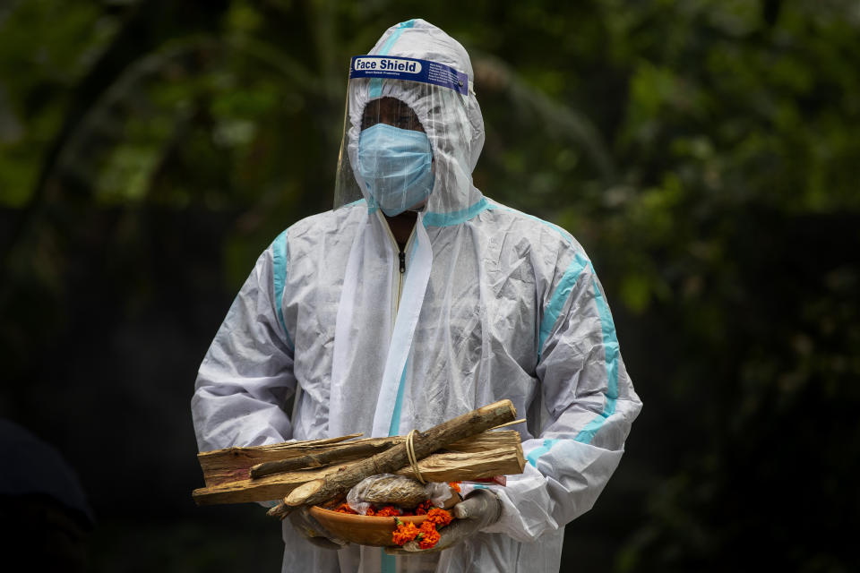 A relative in protective suit waits to perform last rituals near the body of a person who died of COVID-19 during cremation in Gauhati, India, Monday, May 24, 2021. India crossed another grim milestone Monday of more than 300,000 people lost to the coronavirus as a devastating surge of infections appeared to be easing in big cities but was swamping the poorer countryside. (AP Photo/Anupam Nath)