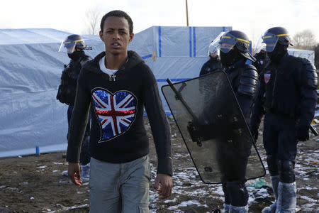 A migrant walks past French riot policemen during the partial dismantlement of the camp for migrants called the "Jungle" in Calais, France, March 7, 2016. REUTERS/Pascal Rossignol